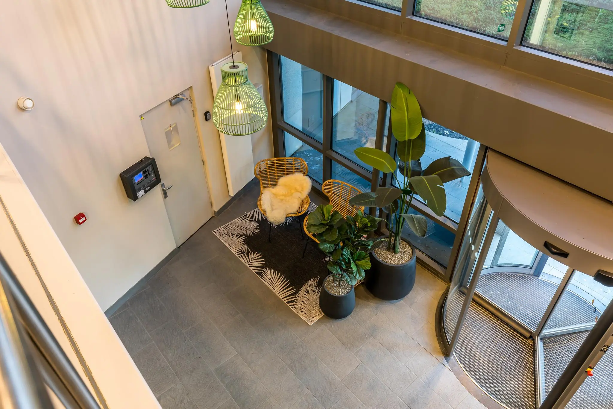 Moderne entreehal aan de Baarnsche Dijk met glazen draaideur, zitje, planten en groen verlichte hanglampen.